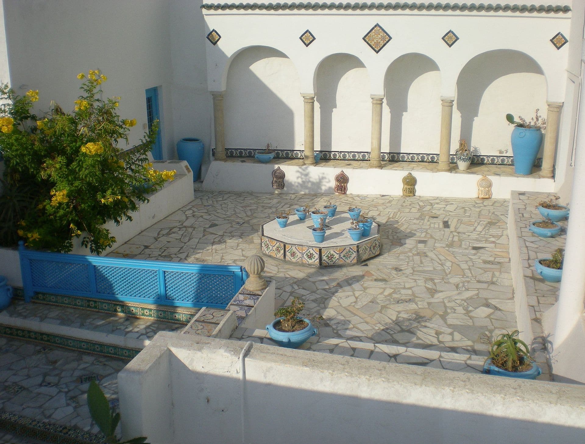 Terrasse-patio aux arcades blanches, jarres bleues, zelliges et fleurs jaunes