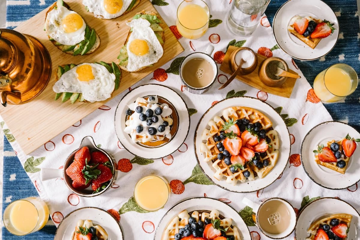 Table du petit-déjeuner : gaufres aux fruits rouges, œufs, jus d'orange et café